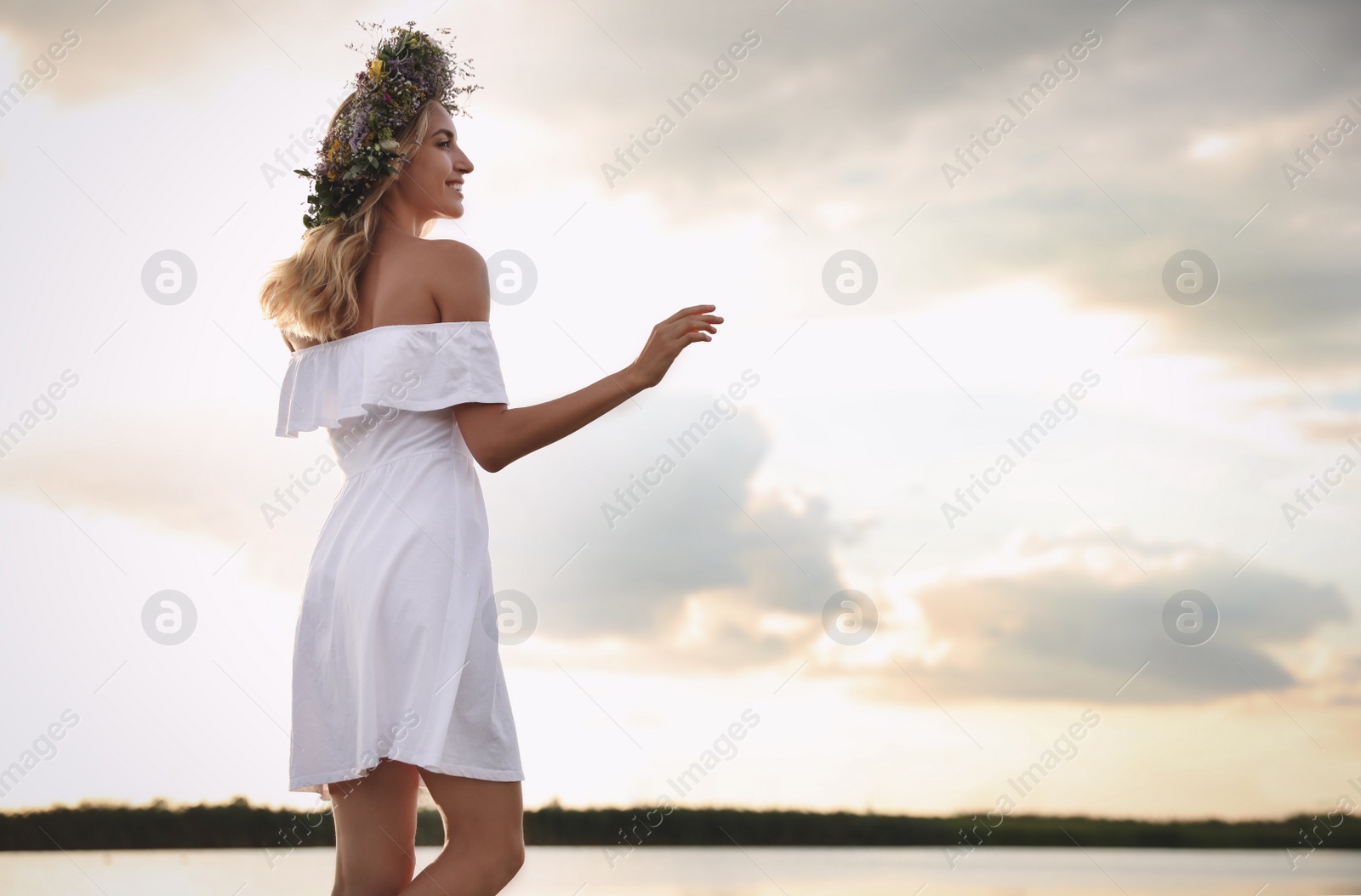 Photo of Young woman wearing wreath made of beautiful flowers near river on sunny day