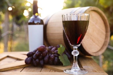 Photo of Composition with wine and ripe grapes on wooden table in vineyard