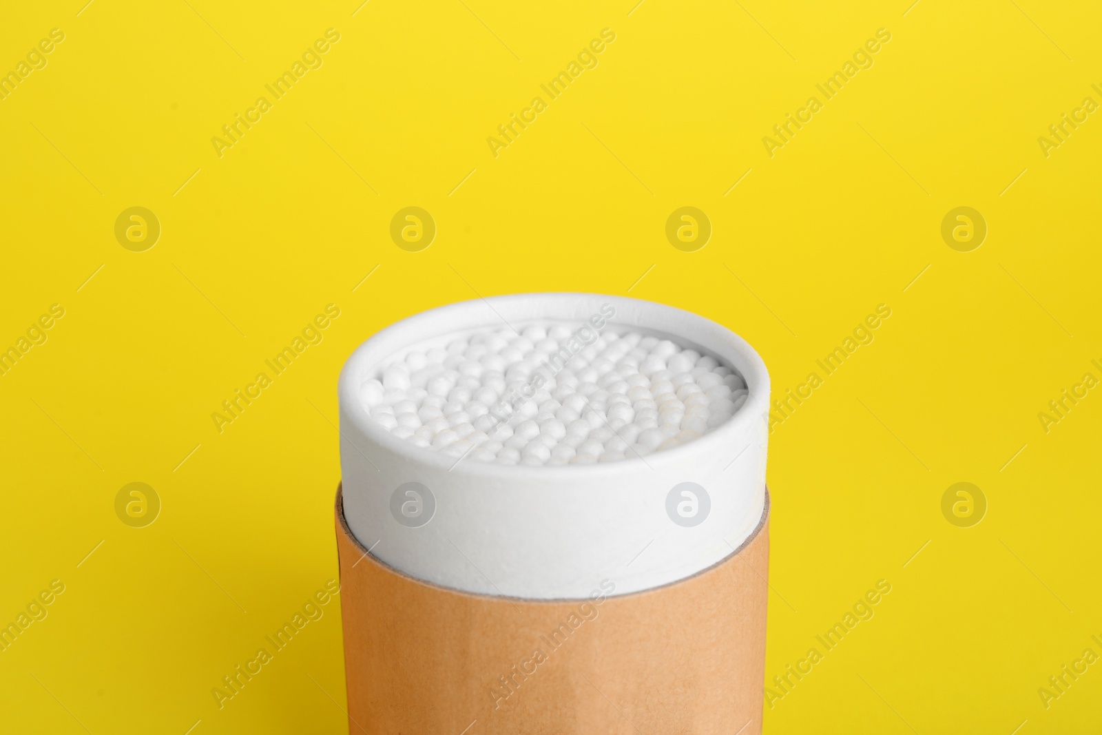 Photo of Container with new cotton buds on yellow background, closeup