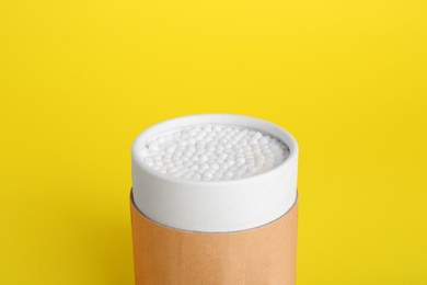 Container with new cotton buds on yellow background, closeup