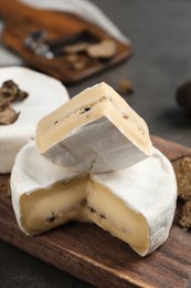 Photo of Wooden board with delicious truffle cheese on grey table, closeup