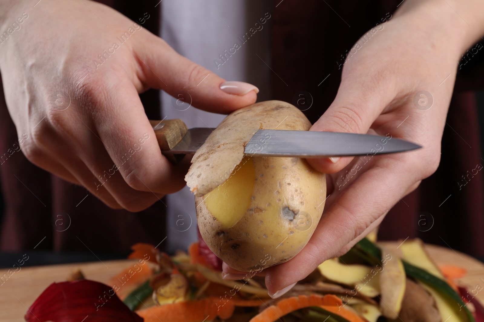 Photo of Woman peeling fresh potato with knife at table, closeup