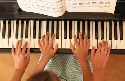 Young woman teaching little girl to play piano indoors, top view