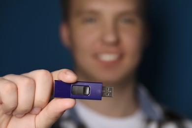 Photo of Man with usb flash drive against blue background, focus on device. Space for text