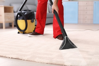 Male worker cleaning carpet with vacuum in living room