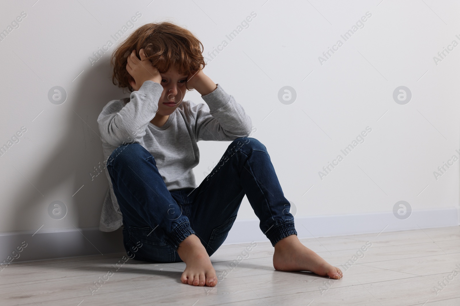 Photo of Child abuse. Upset boy sitting on floor near white wall, space for text