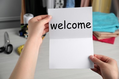 Image of Seamstress paper with word Welcome at table in atelier, closeup