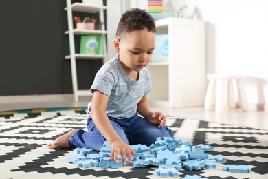 Photo of Cute little African-American child playing with puzzles on floor in kindergarten. Indoor activity