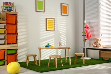 Stylish playroom interior with wooden table and stools