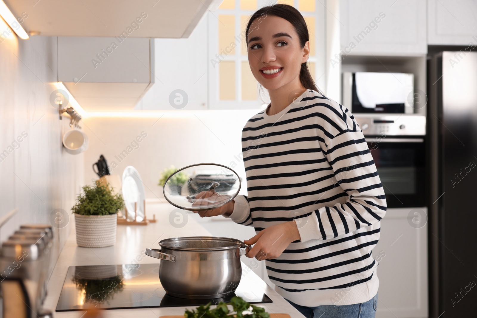 Photo of Smiling woman with lid cooking soup in kitchen