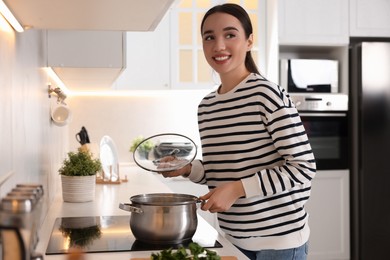 Smiling woman with lid cooking soup in kitchen