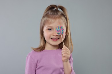 Happy girl covering eye with lollipop on light grey background