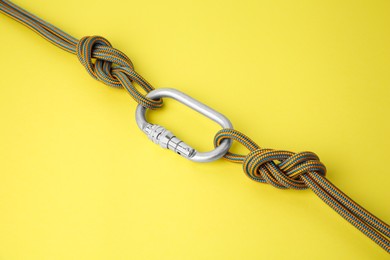 Photo of One metal carabiner with ropes on yellow background