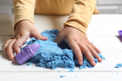 Photo of Little child playing with light blue kinetic sand at white wooden table, closeup