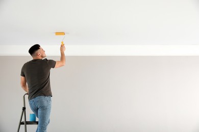 Man painting ceiling with roller in room, back view. Space for text