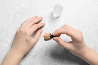 Photo of Woman dripping serum from pipette on her hand at light grey marble table, top view
