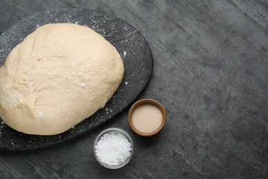 Fresh yeast dough and ingredients on black table, flat lay. Space for text