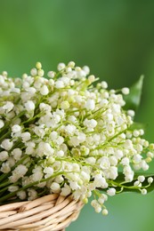 Photo of Wicker basket with beautiful lily of the valley flowers on blurred green background, closeup