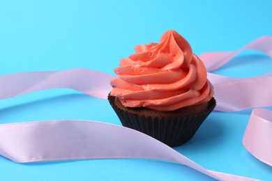 Delicious cupcake with bright cream and ribbon on light blue background