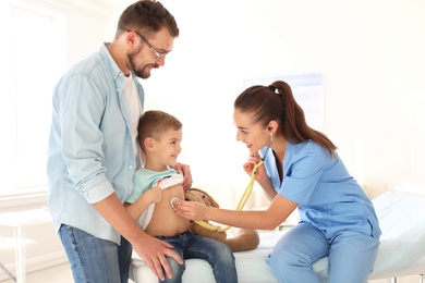 Children's doctor examining little boy with stethoscope in hospital