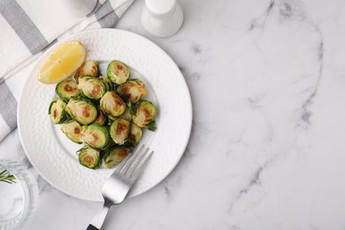 Photo of Delicious roasted Brussels sprouts, slice of lemon and fork on white marble table, top view. Space for text
