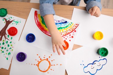 Photo of Little child painting with finger at wooden table indoors, top view