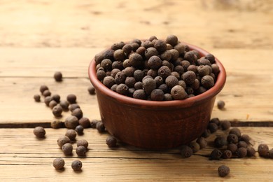 Photo of Aromatic allspice pepper grains in bowl on wooden table