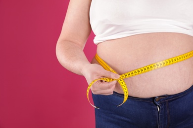 Photo of Overweight woman measuring waist with tape on color background, closeup. Space for text