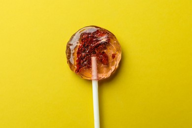 Photo of Sweet colorful lollipop with berries on yellow background, top view