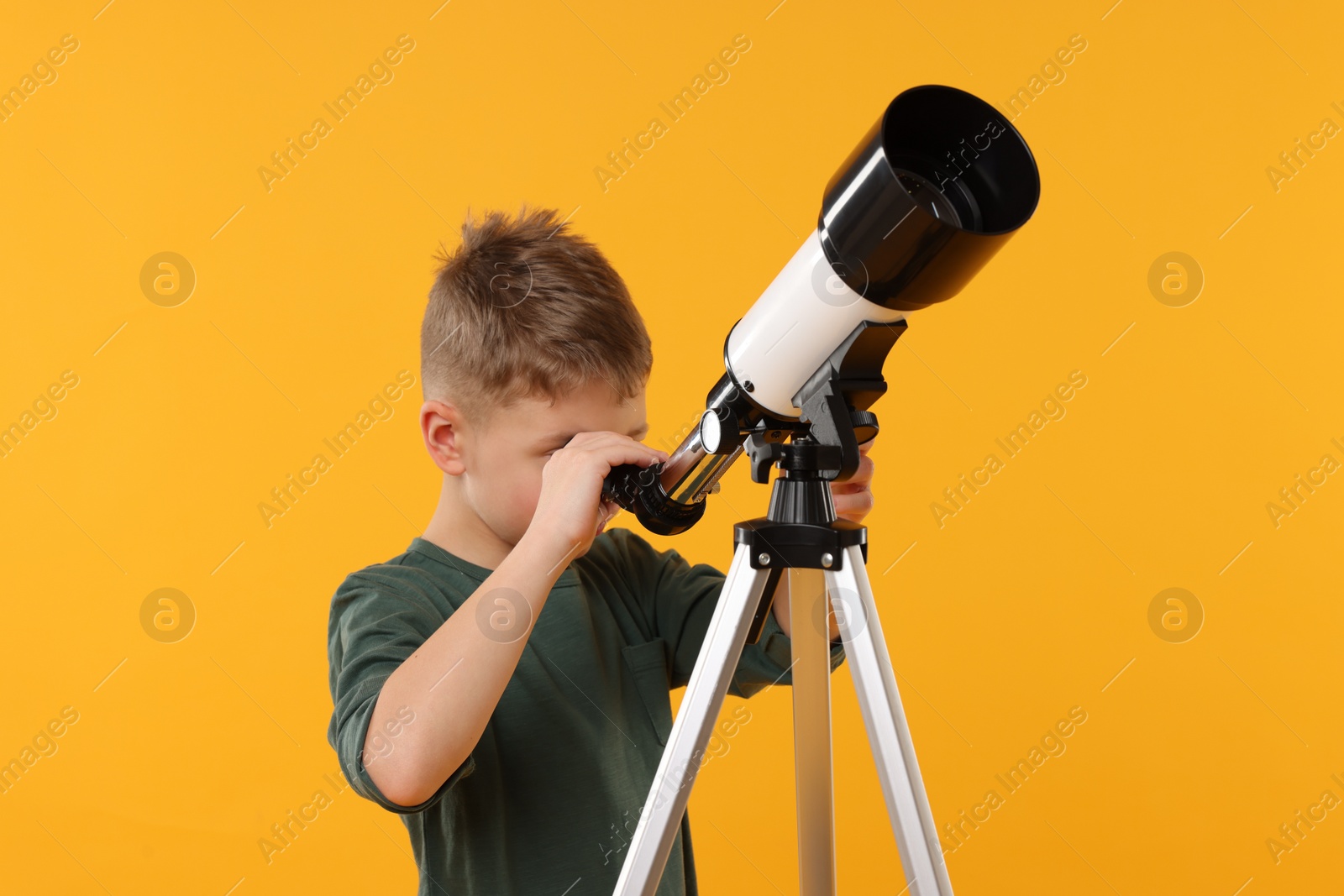 Photo of Little boy looking at stars through telescope on orange background