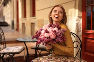 Beautiful woman with bouquet of spring flowers in outdoor cafe, space for text