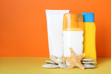 Different suntan products, starfish and stones on color background. Space for text