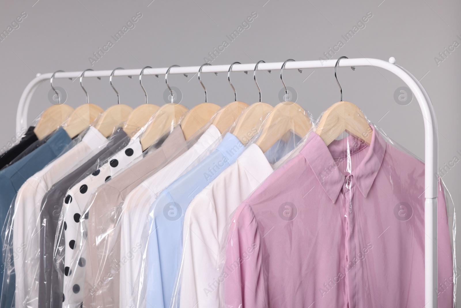 Photo of Dry-cleaning service. Many different clothes in plastic bags hanging on rack against grey background