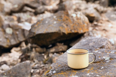 Photo of Metal mug on rock outdoors. Camping season