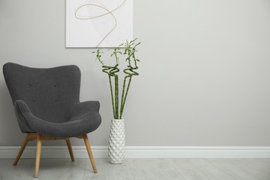 Vase with green bamboo stems and stylish armchair in room, space for text. Interior design