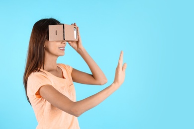 Young woman using cardboard virtual reality headset on color background. Space for text