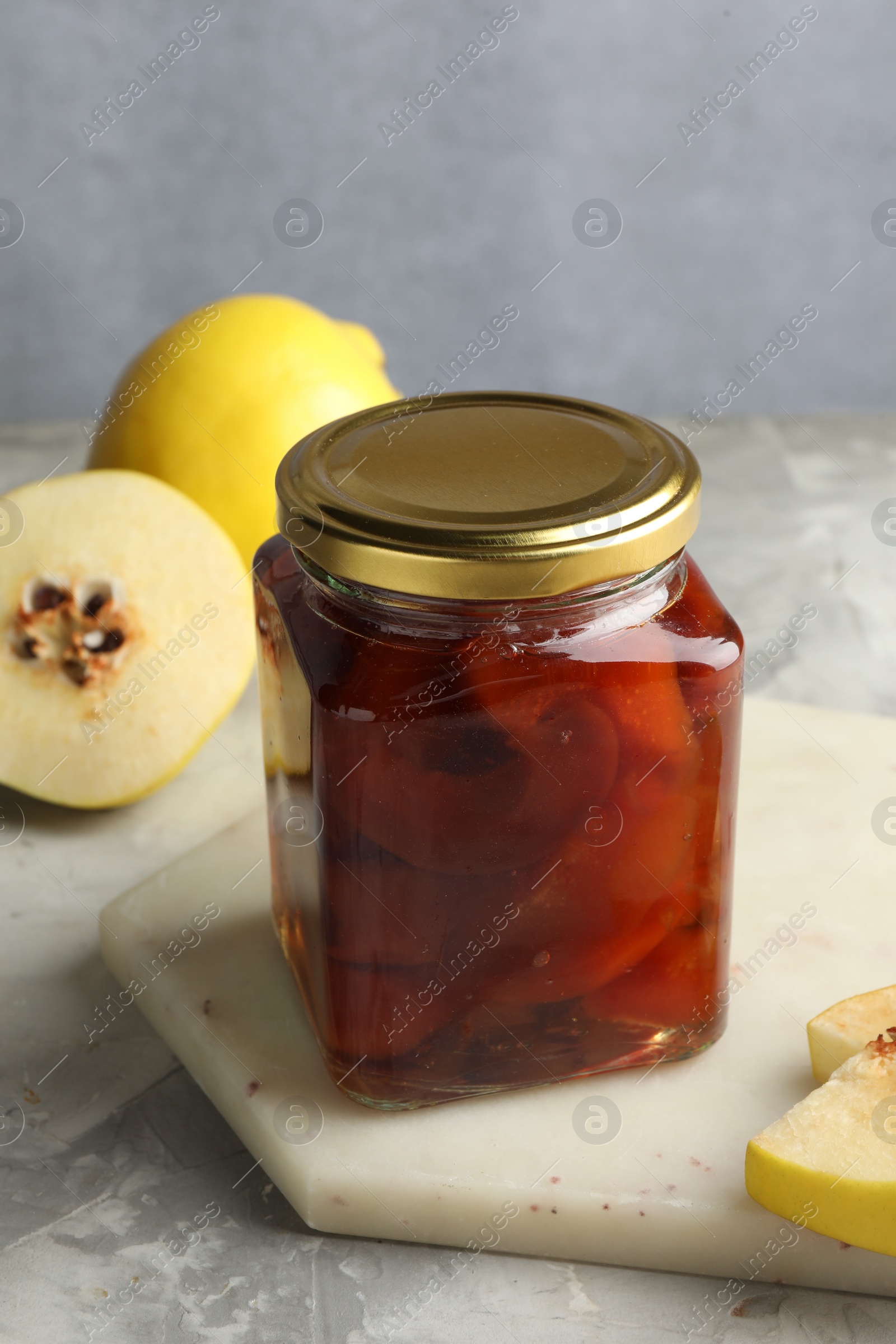 Photo of Tasty homemade quince jam in jar and fruits on grey textured table