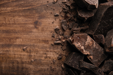 Photo of Pieces of dark chocolate on wooden table, flat lay. Space for text