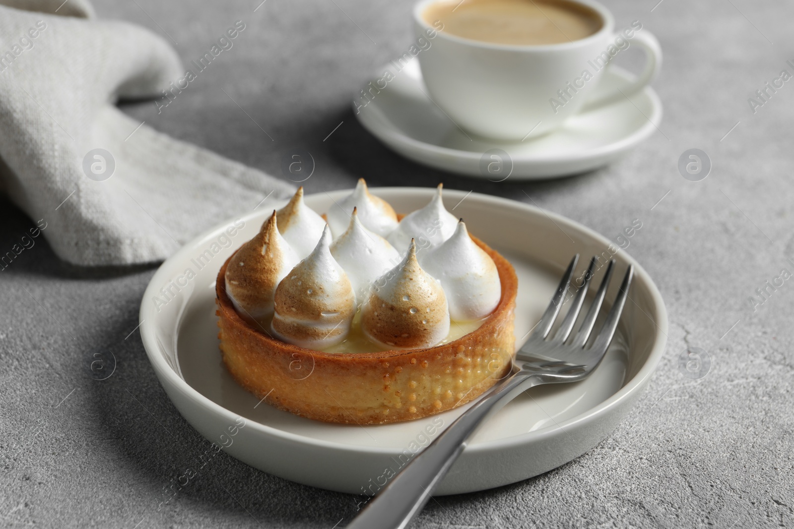 Photo of Tartlet with meringue served on light grey table, closeup. Tasty dessert