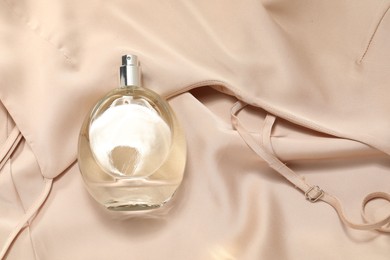 Photo of Luxury perfume in bottle on beige silk fabric, top view