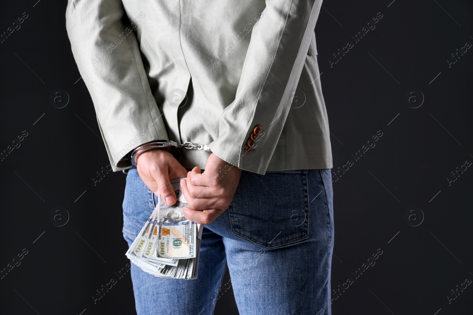 Photo of Man in handcuffs holding bribe money on black background, closeup