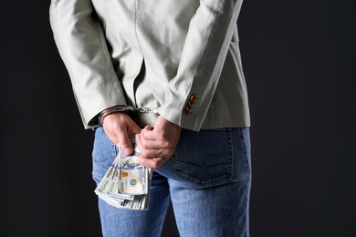 Photo of Man in handcuffs holding bribe money on black background, closeup