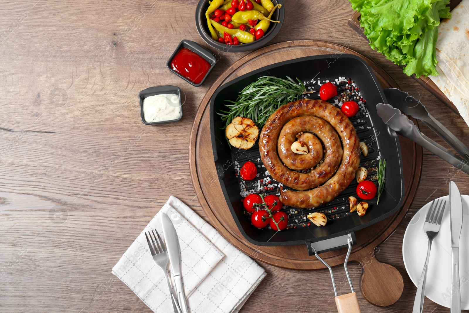 Photo of Delicious homemade sausage with garlic, tomatoes, rosemary and spices served on wooden table, flat lay. Space for text