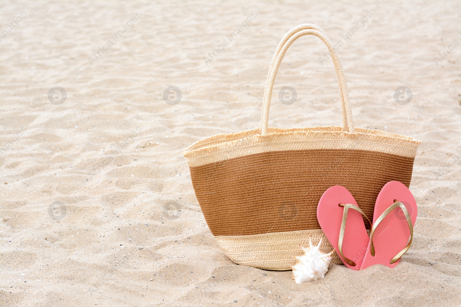Photo of Stylish straw bag, flip flops and seashell on sand outdoors, space for text. Beach accessories