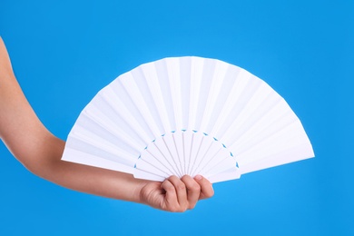 Photo of Woman holding white hand fan on light blue background, closeup