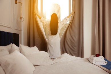 Image of Young woman opening window curtains in hotel room, back view