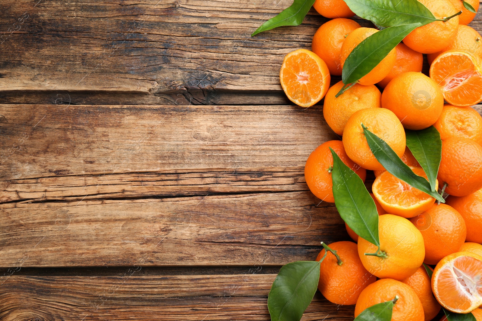 Photo of Fresh ripe tangerines with green leaves on wooden table, flat lay. Space for text