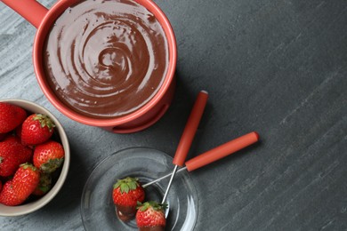 Fondue pot with melted chocolate, fresh strawberries and forks on grey table, flat lay. Space for text