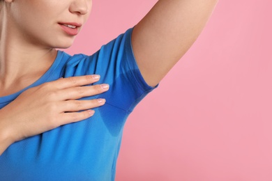 Photo of Young woman with sweat stain on her clothes against pink background, closeup. Using deodorant