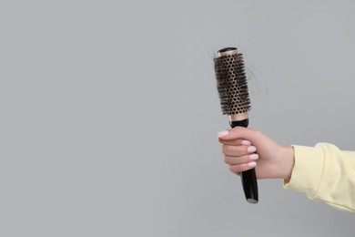 Woman holding brush with lost hair on grey background, closeup and space for text. Alopecia problem